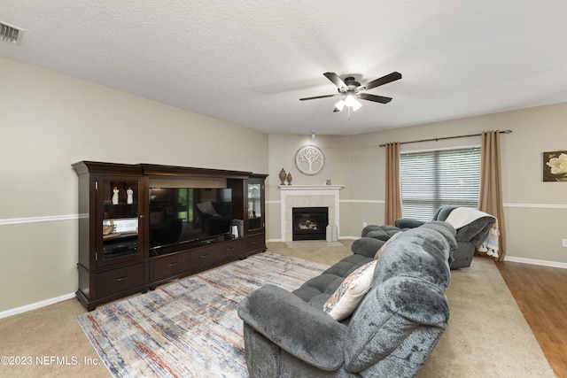 living room with ceiling fan, a textured ceiling, and a fireplace