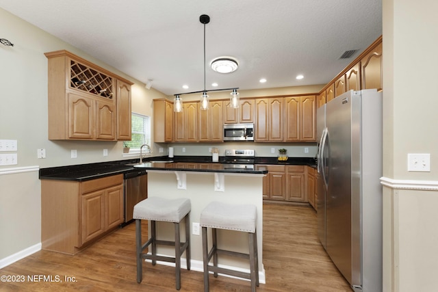 kitchen with a kitchen bar, light hardwood / wood-style flooring, hanging light fixtures, a kitchen island, and appliances with stainless steel finishes