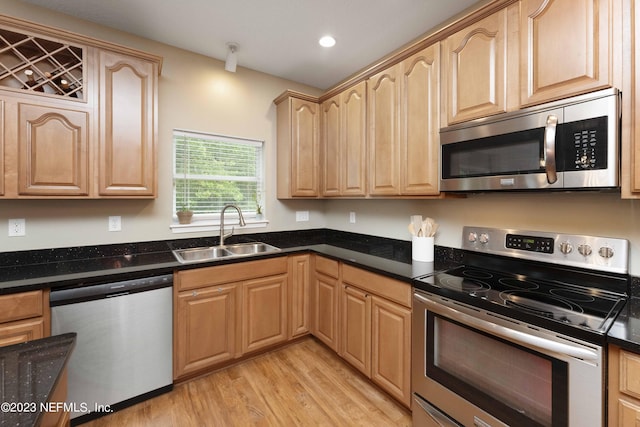 kitchen with sink, light wood-type flooring, dark stone counters, appliances with stainless steel finishes, and light brown cabinets