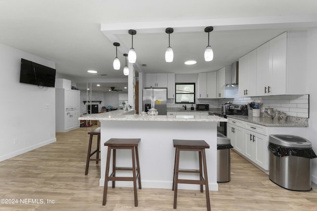 kitchen featuring a kitchen island, white cabinetry, wall chimney range hood, and appliances with stainless steel finishes