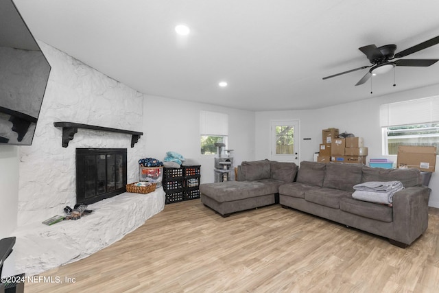 living room with a fireplace, ceiling fan, and light wood-type flooring