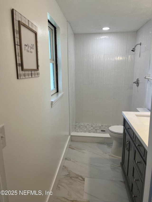 bathroom with tiled shower, vanity, and toilet