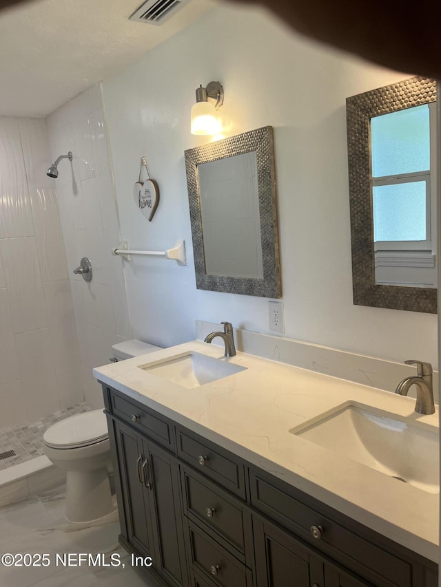 bathroom with tiled shower, vanity, and toilet