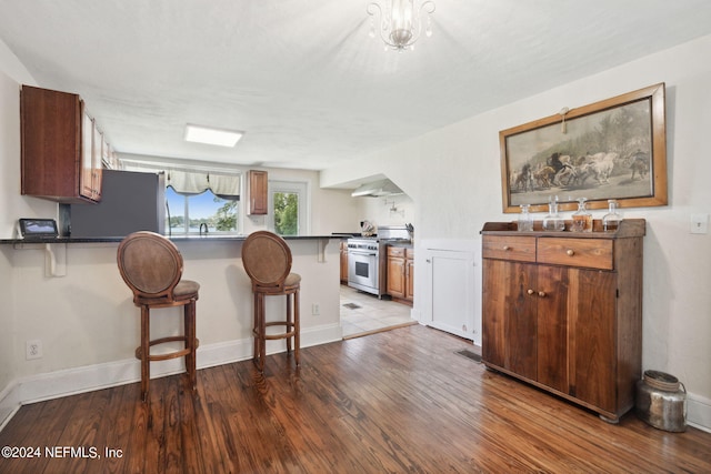 kitchen with a breakfast bar area, refrigerator, a peninsula, wood finished floors, and high end stainless steel range