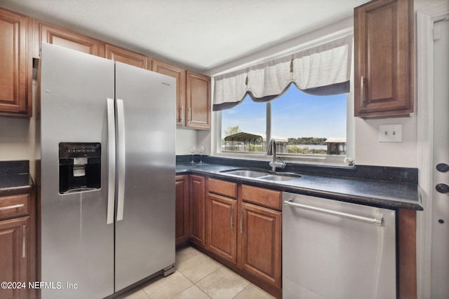 kitchen with brown cabinetry, dark countertops, stainless steel appliances, a sink, and light tile patterned flooring