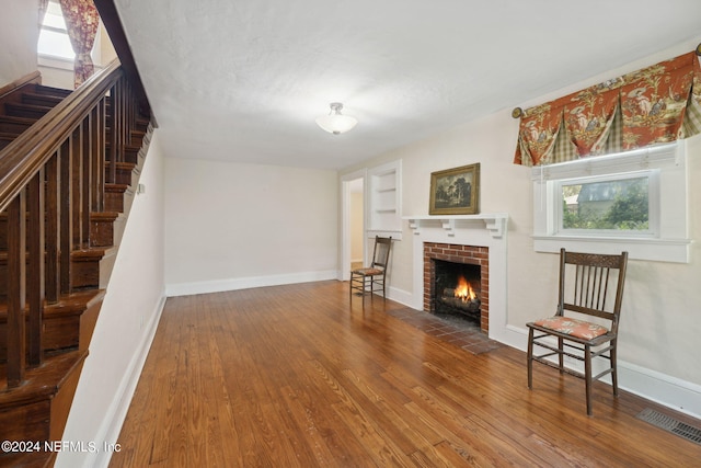 living room featuring a brick fireplace, baseboards, visible vents, and wood finished floors