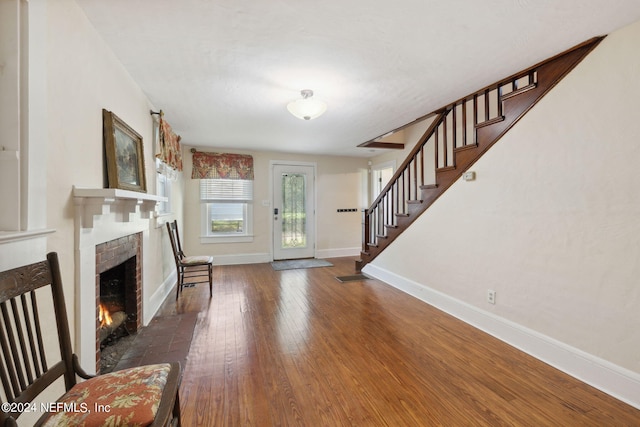 foyer entrance featuring baseboards, visible vents, hardwood / wood-style flooring, stairway, and a brick fireplace