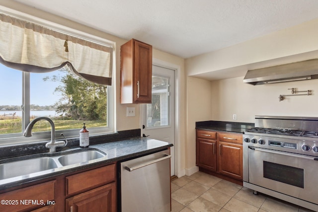 kitchen with stainless steel appliances, light tile patterned flooring, a sink, ventilation hood, and dark stone counters