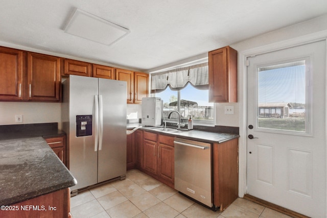 kitchen with appliances with stainless steel finishes, brown cabinets, a sink, and light tile patterned floors