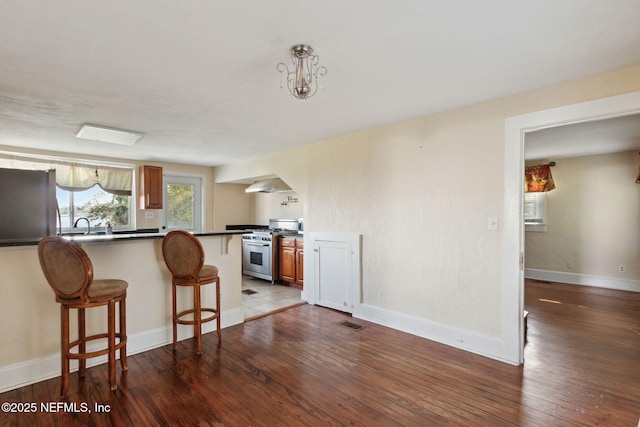 kitchen with hardwood / wood-style flooring, a kitchen breakfast bar, appliances with stainless steel finishes, wall chimney range hood, and dark countertops