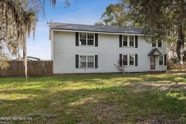 rear view of house featuring a lawn and fence