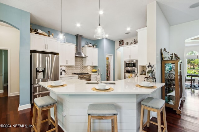 kitchen with pendant lighting, stainless steel appliances, a kitchen breakfast bar, and wall chimney exhaust hood