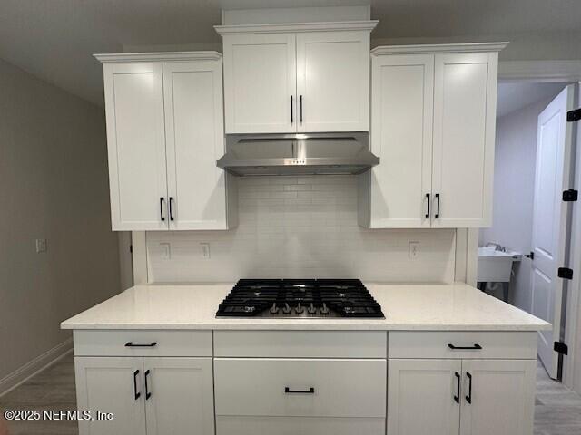 kitchen with backsplash, white cabinets, under cabinet range hood, and gas cooktop