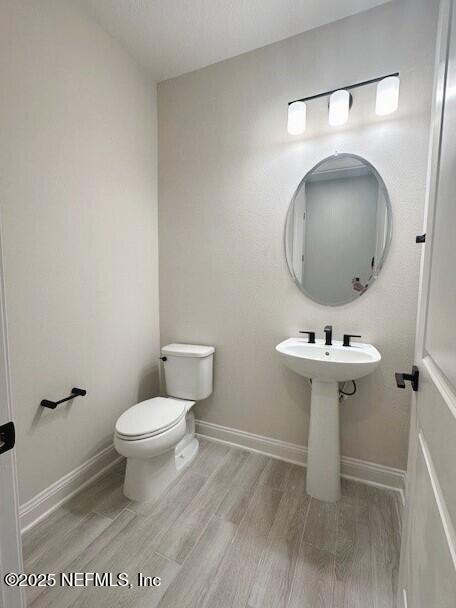 bathroom with toilet, baseboards, and wood finished floors