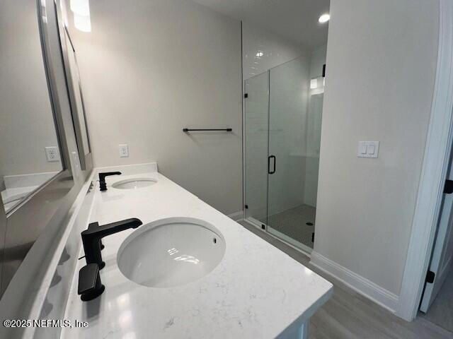 bathroom with a sink, double vanity, a shower stall, and baseboards