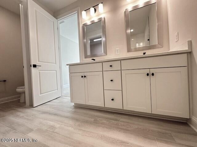 bathroom with double vanity, baseboards, toilet, and wood finished floors