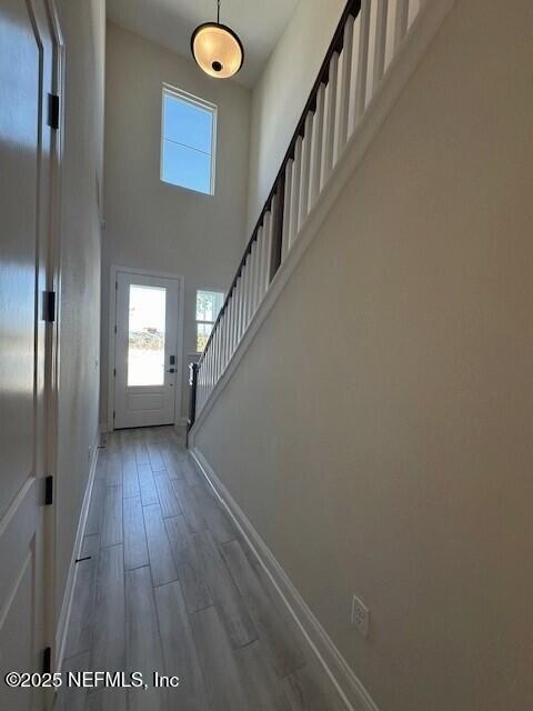 doorway with stairs, a high ceiling, baseboards, and wood finished floors