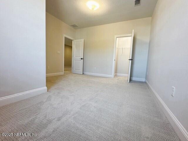 unfurnished bedroom with a closet, light colored carpet, visible vents, and baseboards