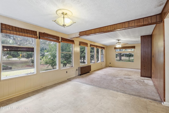 unfurnished living room featuring radiator, ceiling fan, a textured ceiling, light colored carpet, and wood walls