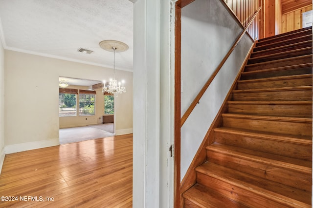 staircase with crown molding, an inviting chandelier, a textured ceiling, and hardwood / wood-style flooring