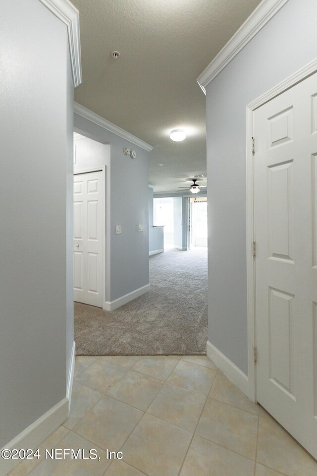 hallway with ornamental molding, a textured ceiling, and light colored carpet