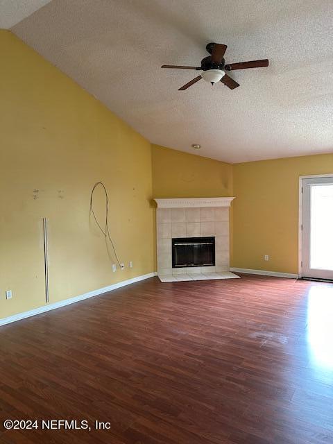 unfurnished living room featuring vaulted ceiling, a fireplace, ceiling fan, wood-type flooring, and a textured ceiling