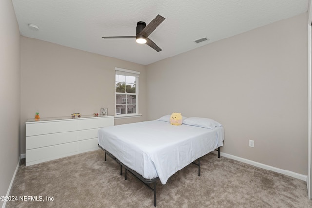 bedroom with ceiling fan, light colored carpet, and a textured ceiling