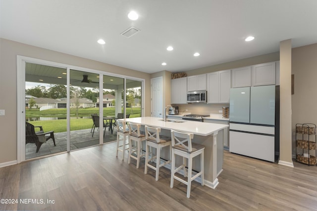 kitchen featuring sink, white fridge, a kitchen island with sink, white cabinets, and range