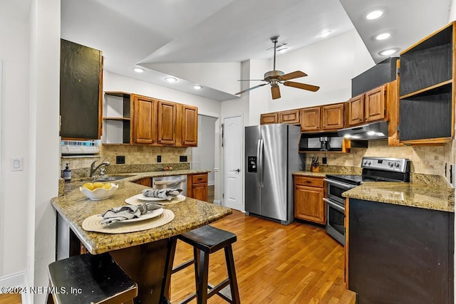 kitchen featuring high vaulted ceiling, sink, a breakfast bar area, light stone counters, and stainless steel appliances