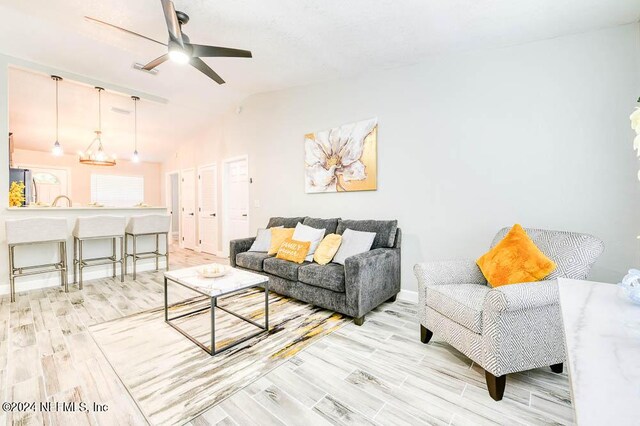 living room featuring light hardwood / wood-style flooring, vaulted ceiling, and ceiling fan with notable chandelier