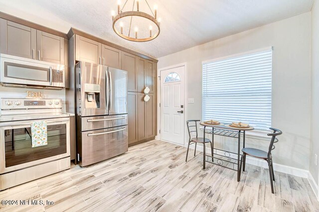 kitchen with stainless steel appliances, light wood-type flooring, a notable chandelier, and a textured ceiling