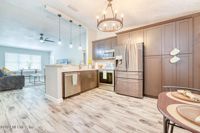 kitchen with a textured ceiling, hanging light fixtures, kitchen peninsula, and appliances with stainless steel finishes