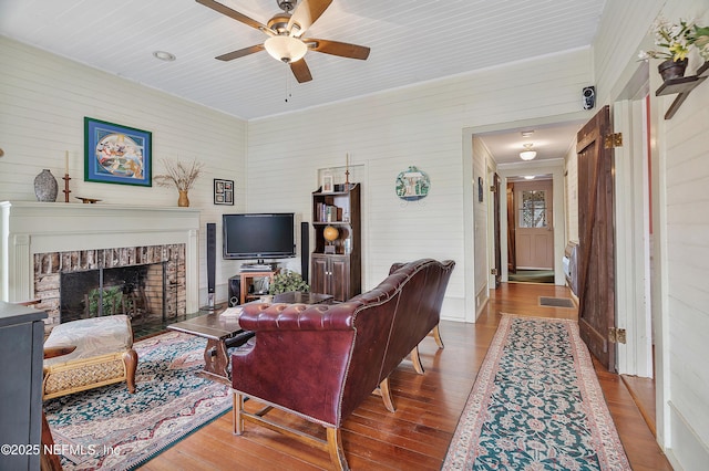 living area featuring a ceiling fan, a brick fireplace, and wood finished floors