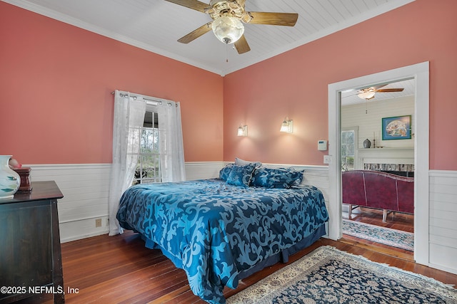 bedroom with a wainscoted wall, crown molding, a ceiling fan, and wood finished floors