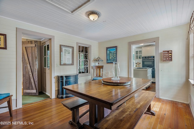 dining room with wooden ceiling, light wood-style flooring, and wooden walls