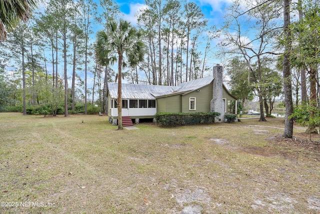 view of property exterior with a yard, a sunroom, metal roof, and a chimney