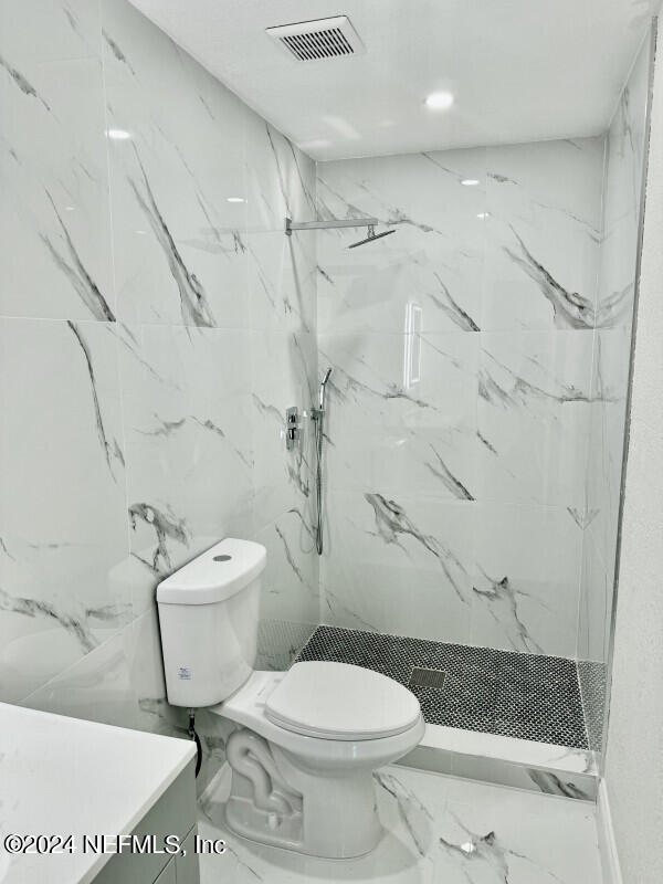 bathroom with toilet, vanity, and a tile shower