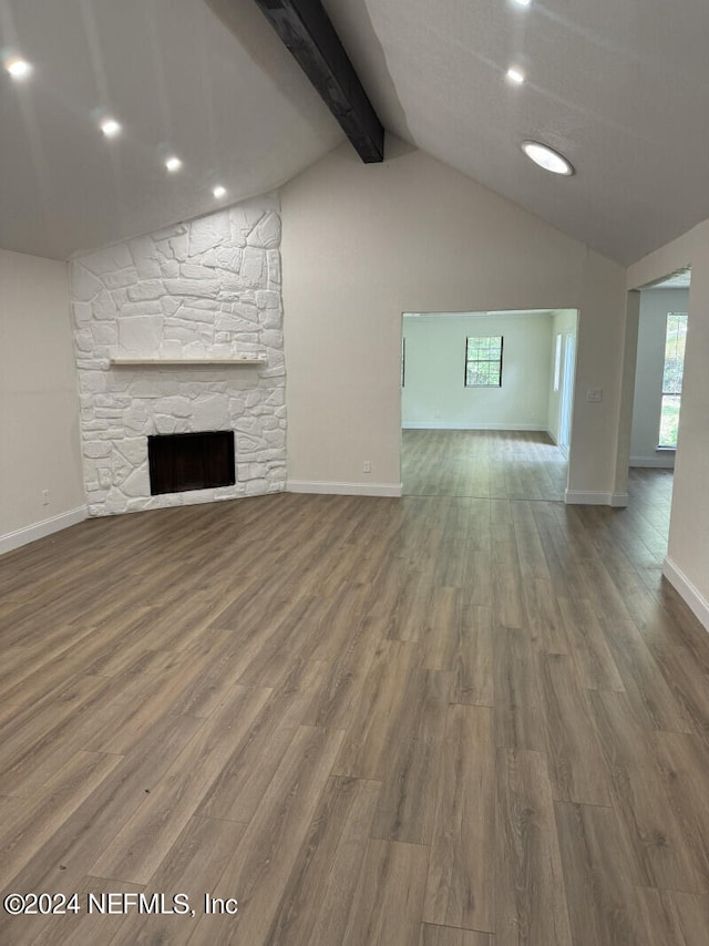 unfurnished living room featuring vaulted ceiling with beams, a stone fireplace, and hardwood / wood-style floors