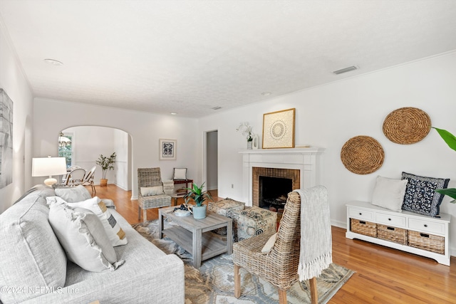 living room featuring a brick fireplace, crown molding, and wood-type flooring