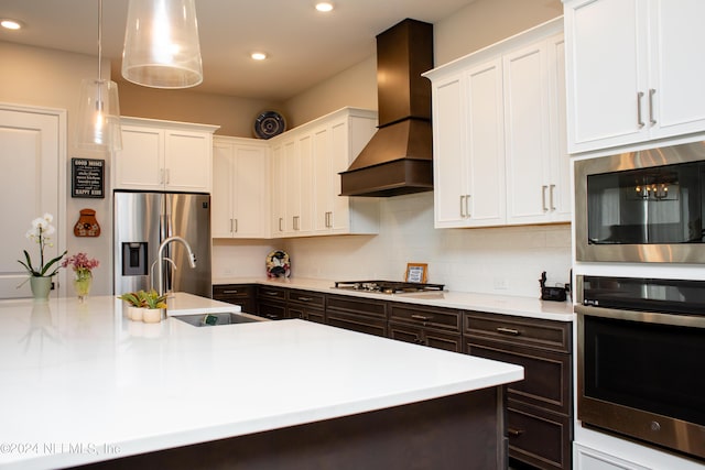 kitchen with appliances with stainless steel finishes, premium range hood, sink, white cabinets, and hanging light fixtures