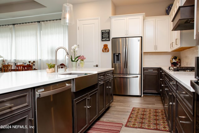 kitchen with white cabinets, hanging light fixtures, decorative backsplash, appliances with stainless steel finishes, and light hardwood / wood-style floors