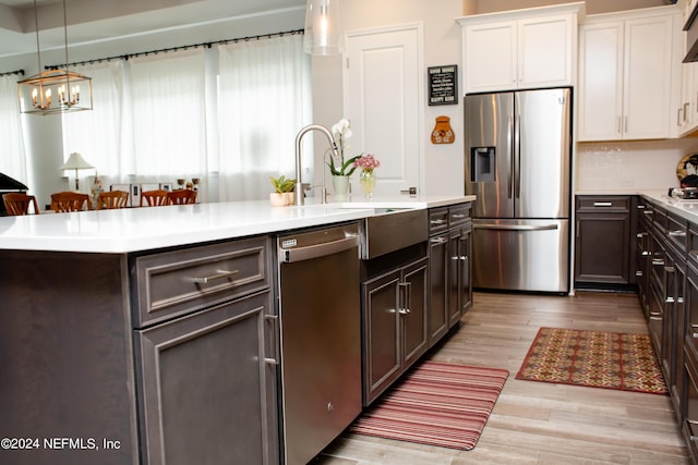 kitchen with appliances with stainless steel finishes, decorative light fixtures, light hardwood / wood-style flooring, a center island with sink, and white cabinetry