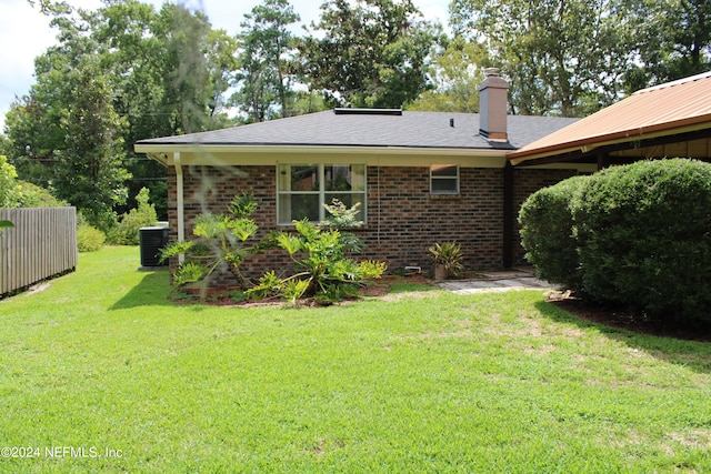 rear view of house with a yard, brick siding, a chimney, and cooling unit