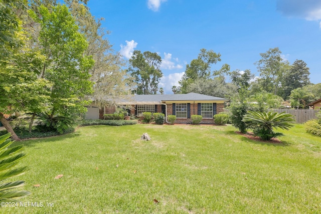 view of front facade featuring a front yard, brick siding, fence, and an attached garage