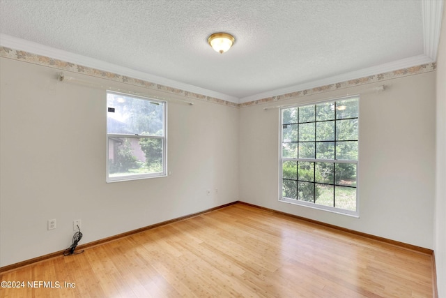 spare room featuring a textured ceiling, ornamental molding, light wood-style flooring, and baseboards