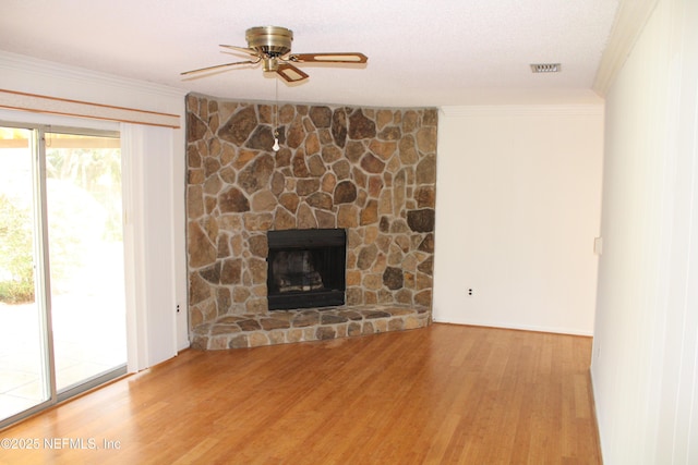 unfurnished living room with visible vents, ornamental molding, ceiling fan, a stone fireplace, and wood finished floors