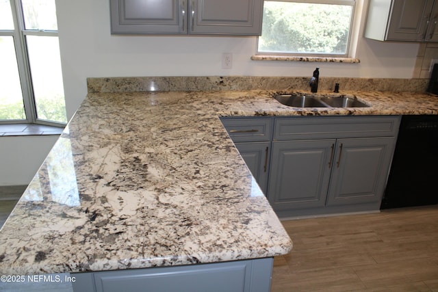 kitchen featuring a sink, light stone counters, dishwasher, and gray cabinetry