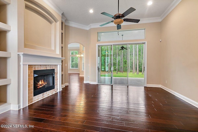 unfurnished living room featuring a tile fireplace, ceiling fan with notable chandelier, crown molding, and dark wood-type flooring