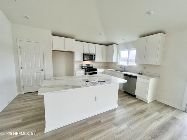 kitchen with stainless steel appliances, light stone countertops, a kitchen island, white cabinets, and sink