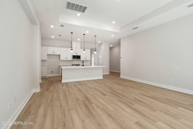 kitchen featuring white cabinets, sink, light hardwood / wood-style flooring, an island with sink, and decorative light fixtures